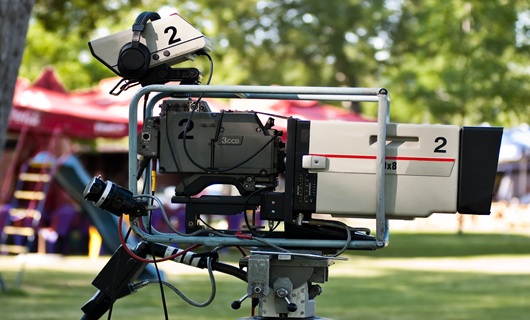 A closeup of a professional video camera on a stand filming a project outdoors on a sunny day